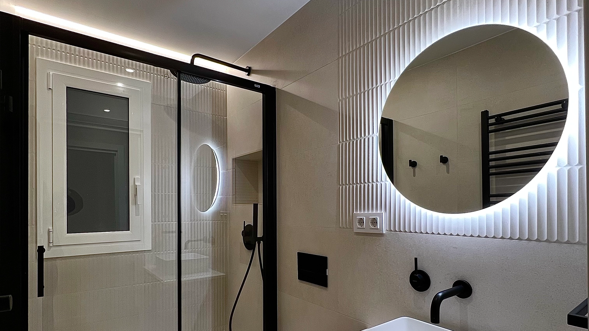 Reforma integral del baño de un piso de Barcelona con espejo redondo retroiluminado.