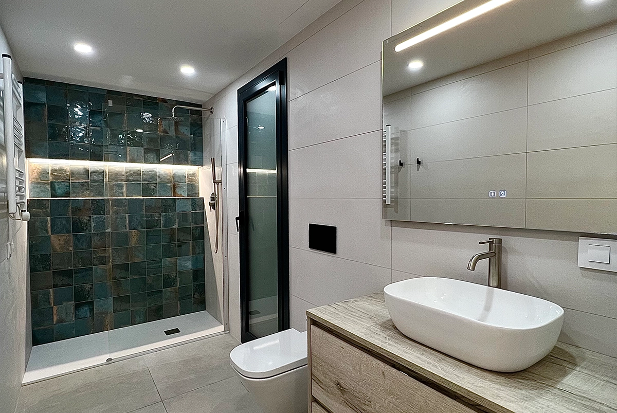 Vista general de baño reformado con gres porcelánico y azulejos vidriados en la ducha.