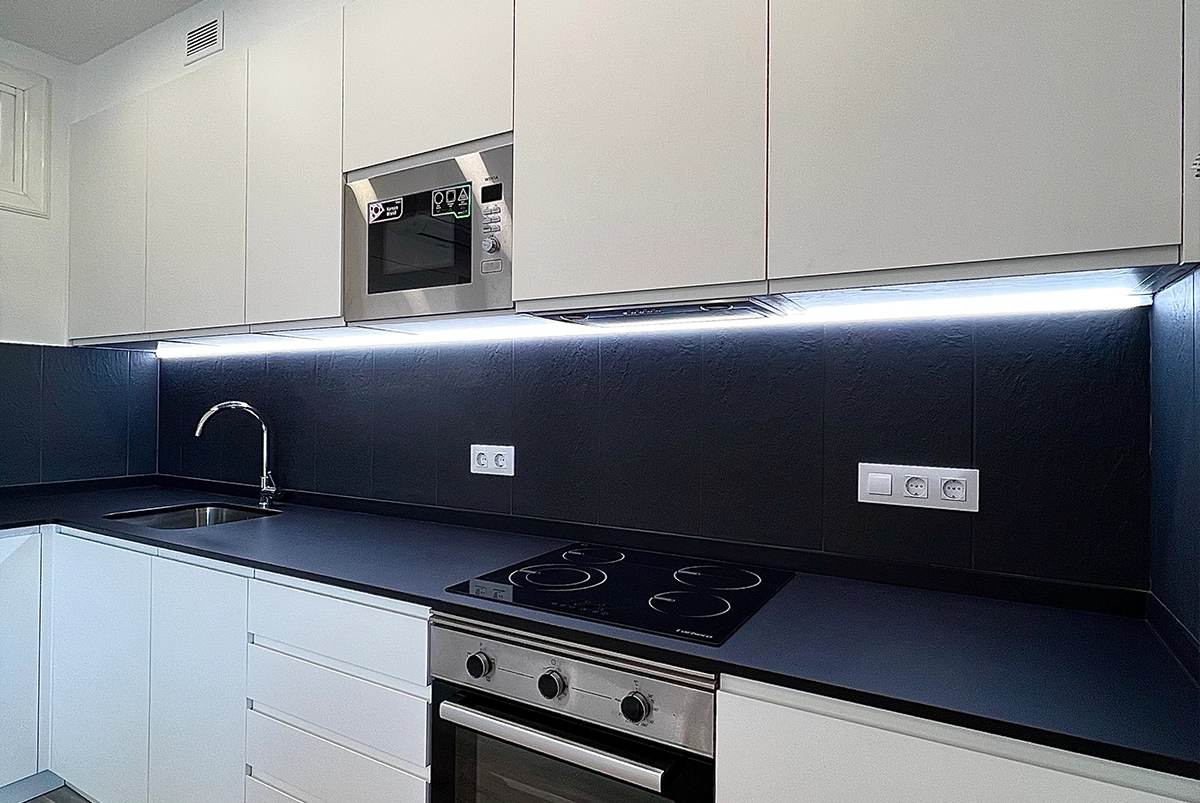 Detalle de iluminación LED en cocina moderna con muebles blancos y encimera negra.