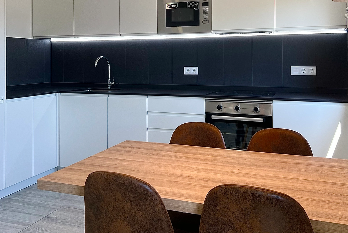 Imagen de cocina moderna abierta con muebles en blanco y encimera y salpicadero en negro.