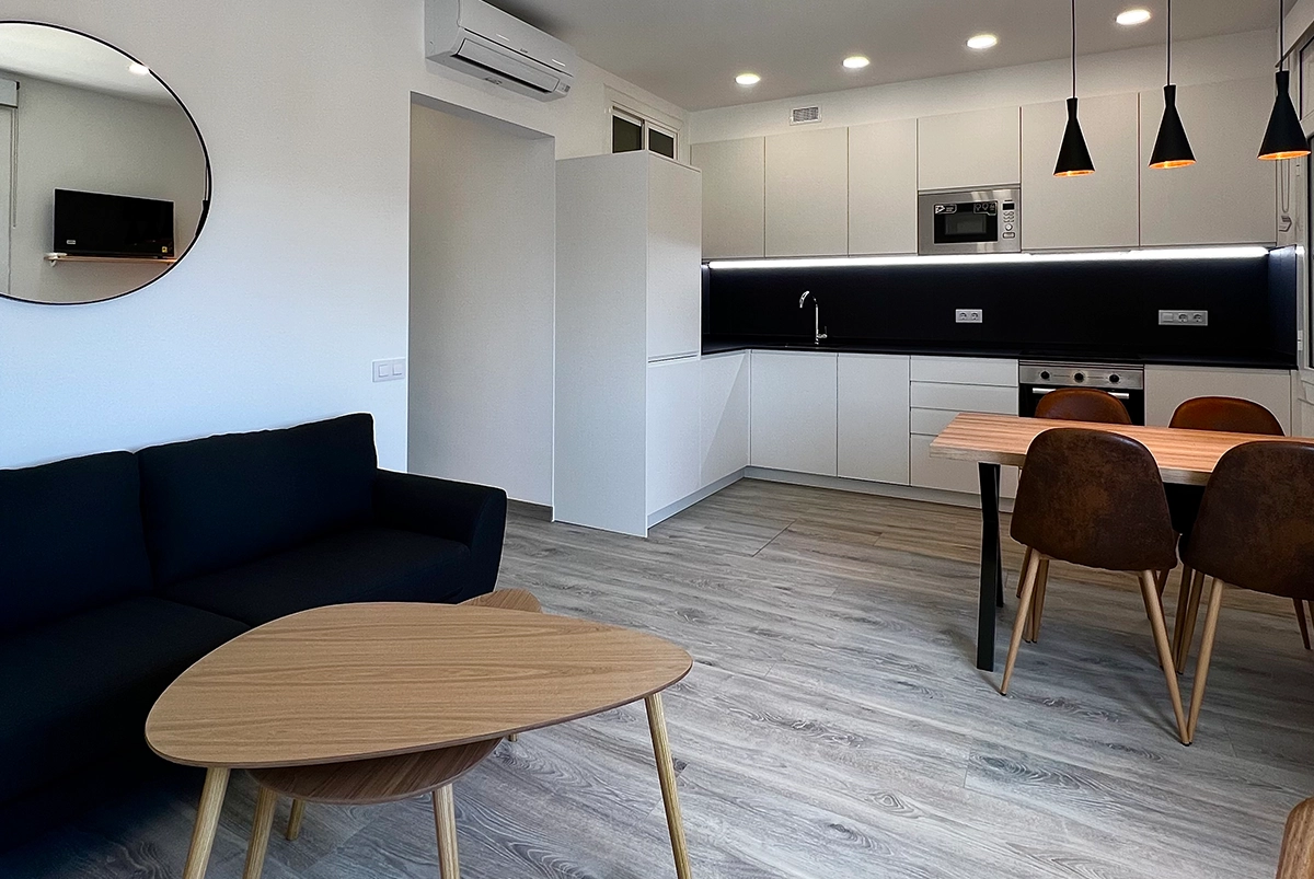 Vista de la reforma de una cocina moderna abierta con muebles blancos y encimera negra.